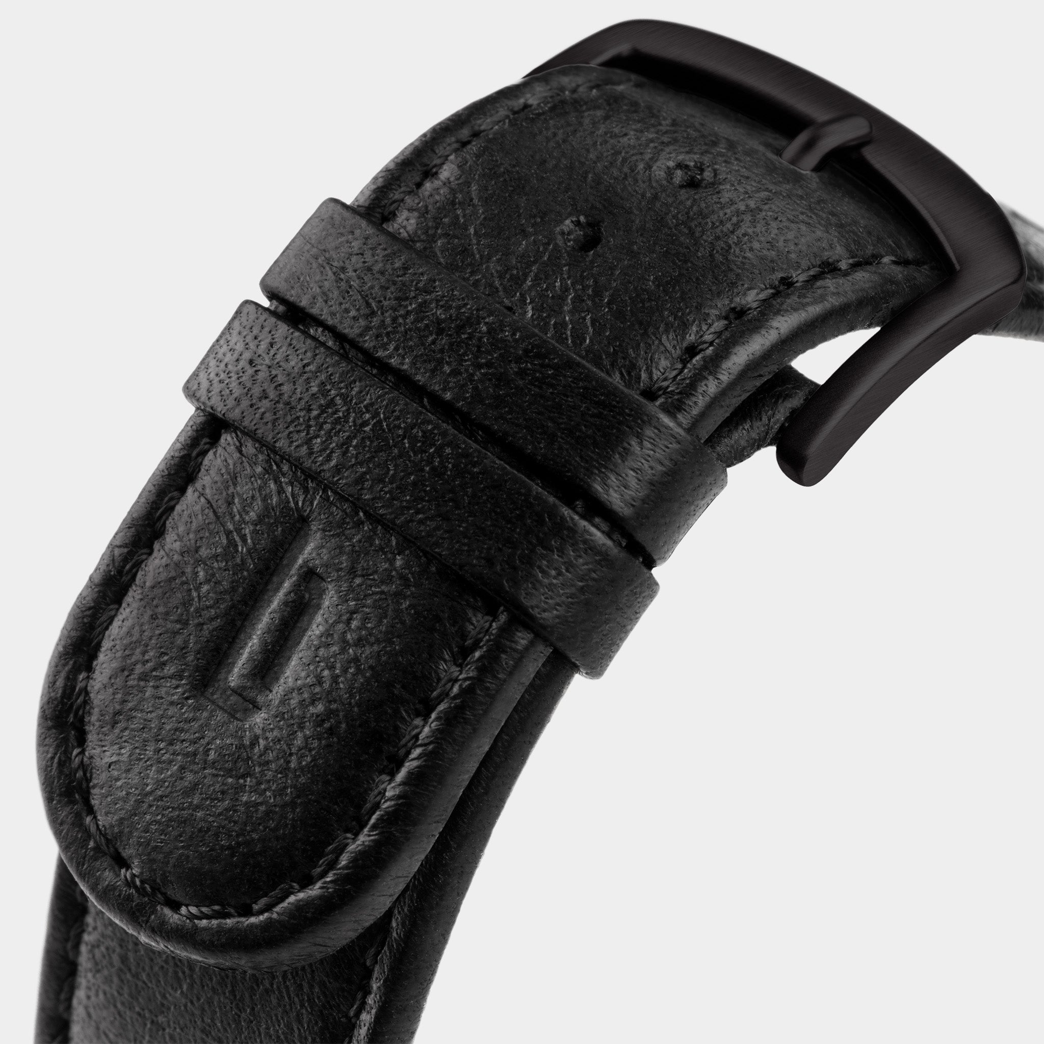 Close-up of a black leather watch strap with matte black buckle and stitched detailing