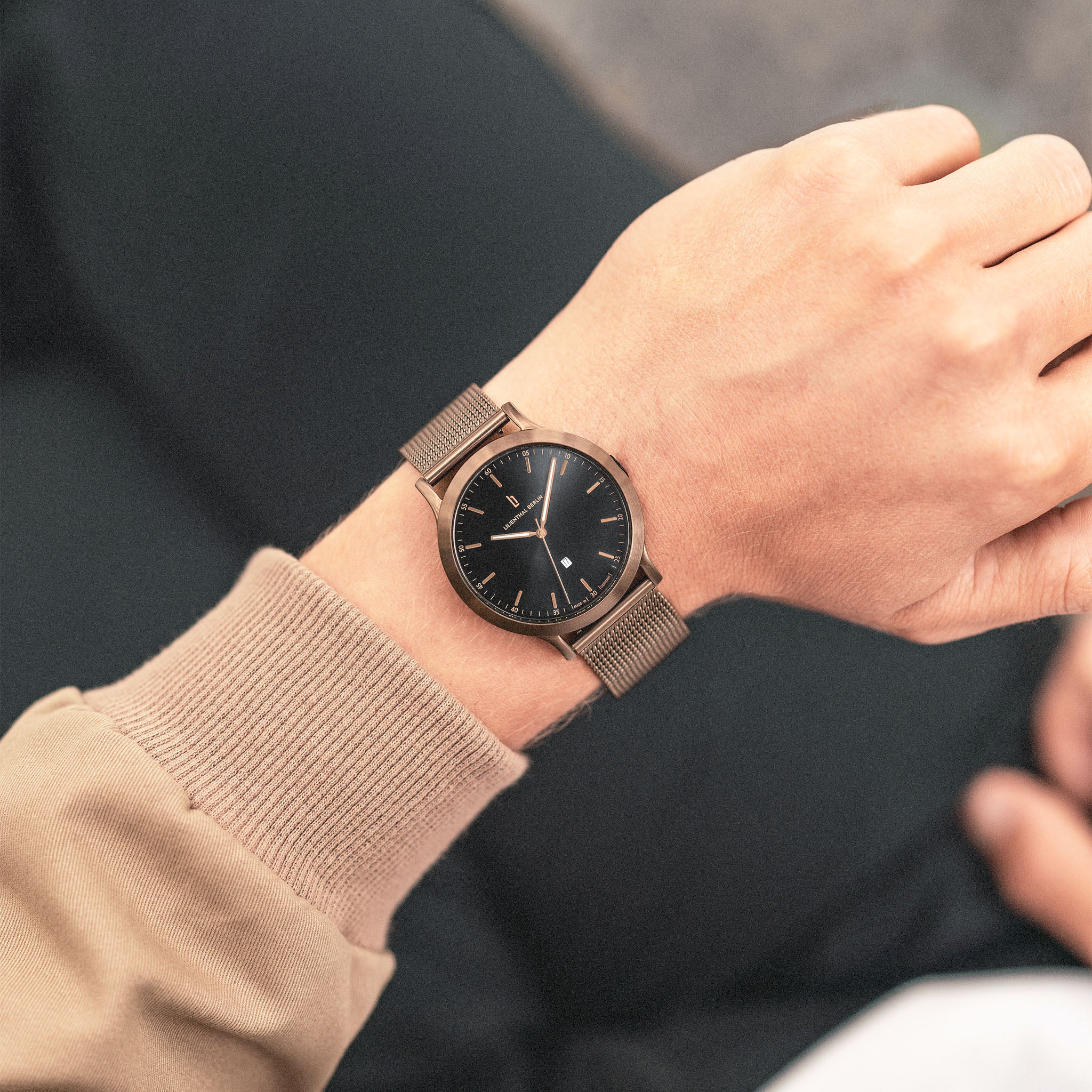 Minimalist gold mesh watch with black dial on person's wrist, modern unisex style