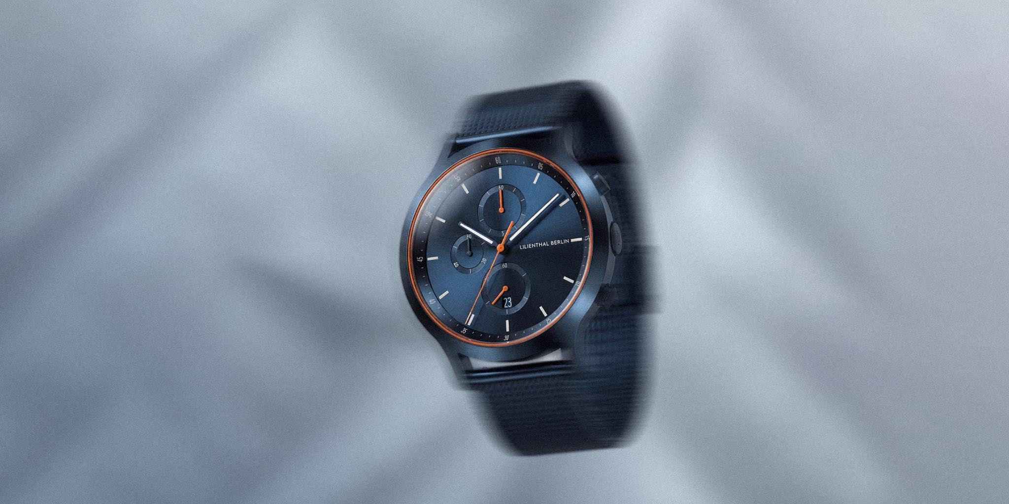 Blue and orange chronograph watch with mesh strap on a light gray background