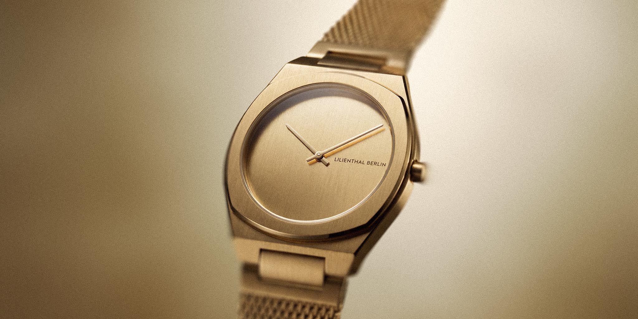 Minimalist gold wristwatch with mesh strap and clean dial on neutral background