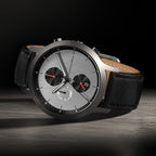 Luxury chronograph wristwatch with silver dial, black subdials, and black leather strap