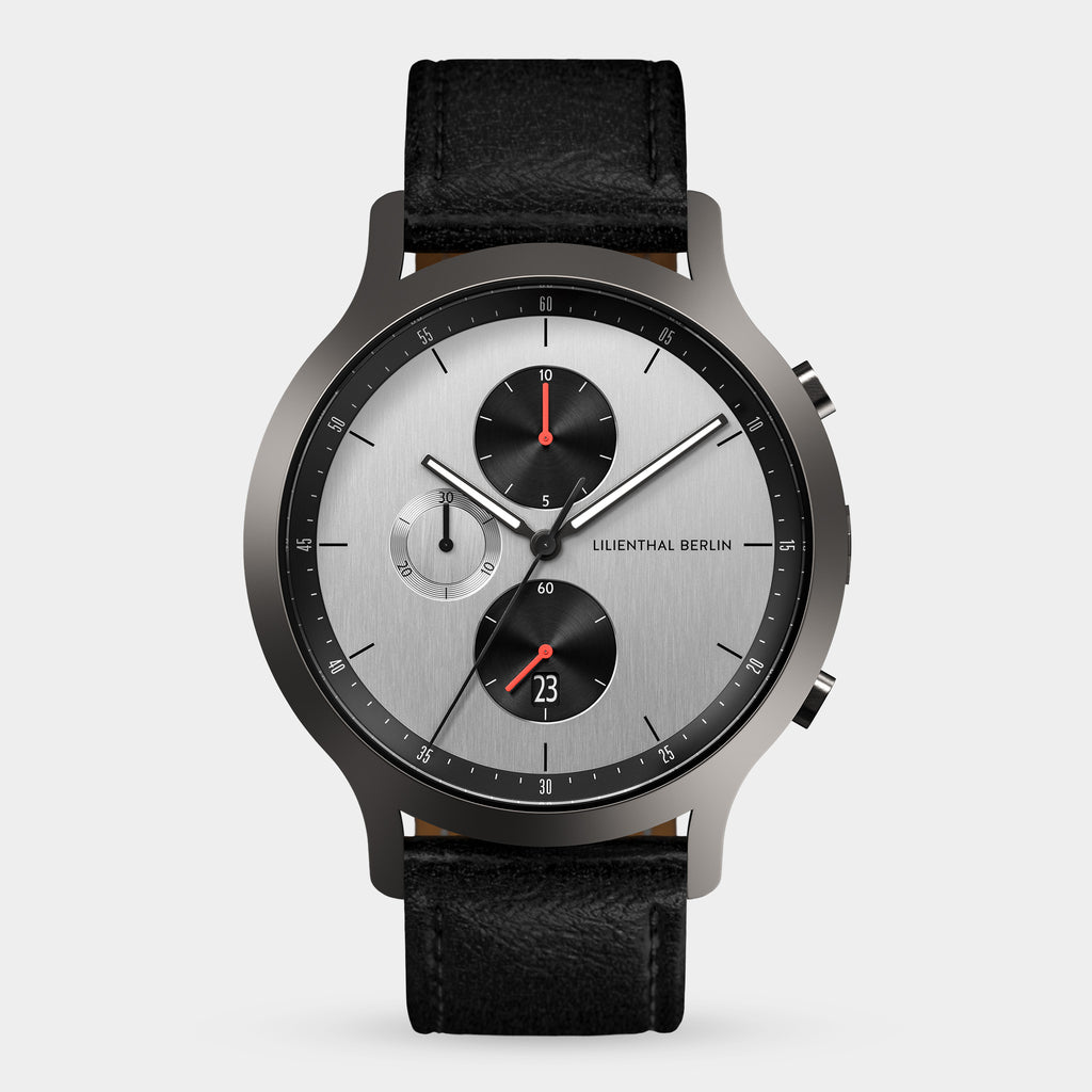 Silver chronograph watch with black leather strap, multi-dial face, and red accents