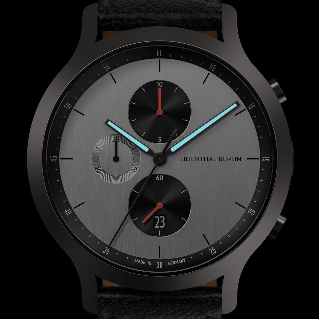 Modern men's chronograph watch with black case, silver dial, subdials, and blue hands