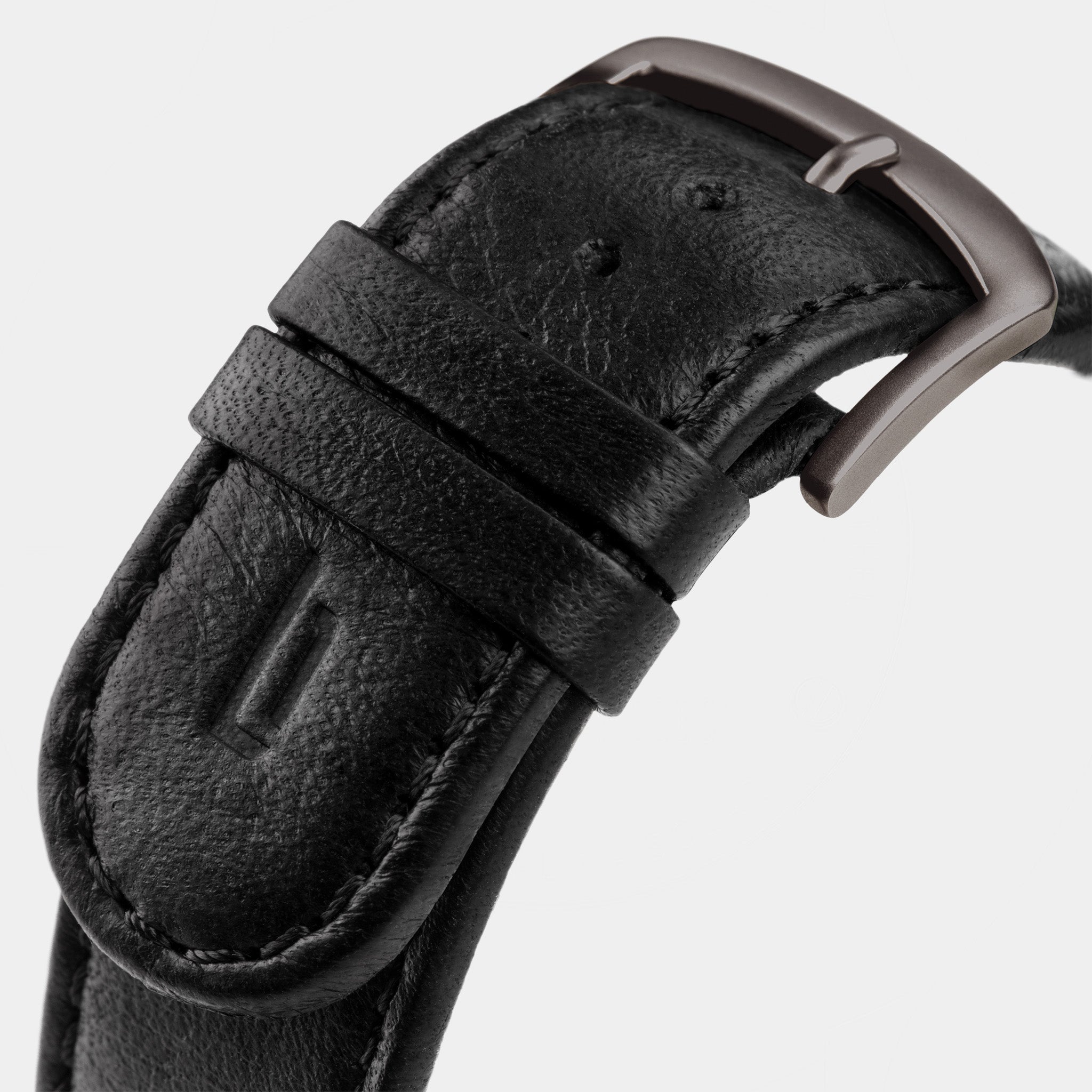 Close-up of a black leather watch strap with a matte metal buckle on a light background