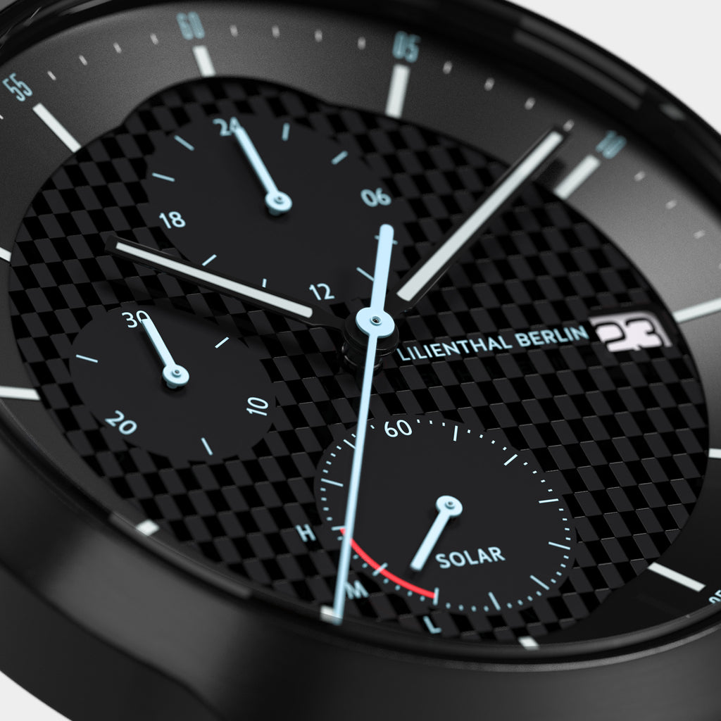 Close-up of a black chronograph watch with carbon fiber dial and luminous blue hands