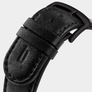 Close-up of a black leather watch strap with matte black buckle and stitched detailing