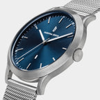 Minimalist silver mesh watch with blue dial and date display on light background