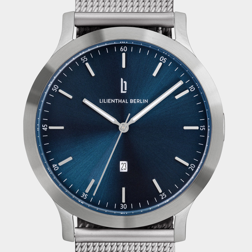 Minimalist steel watch with blue sunray dial, silver mesh strap, and date display