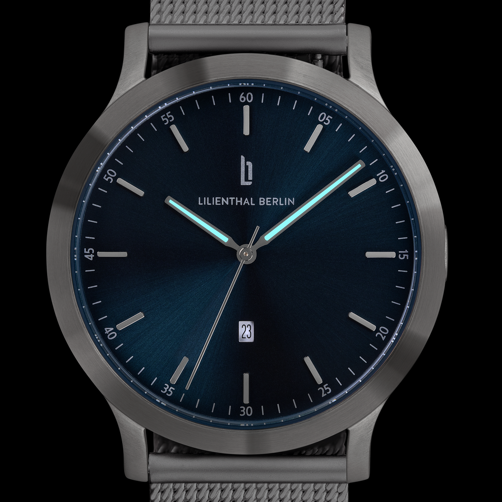 Sleek minimalist wristwatch with dark blue dial, luminous hands, date window, and mesh strap