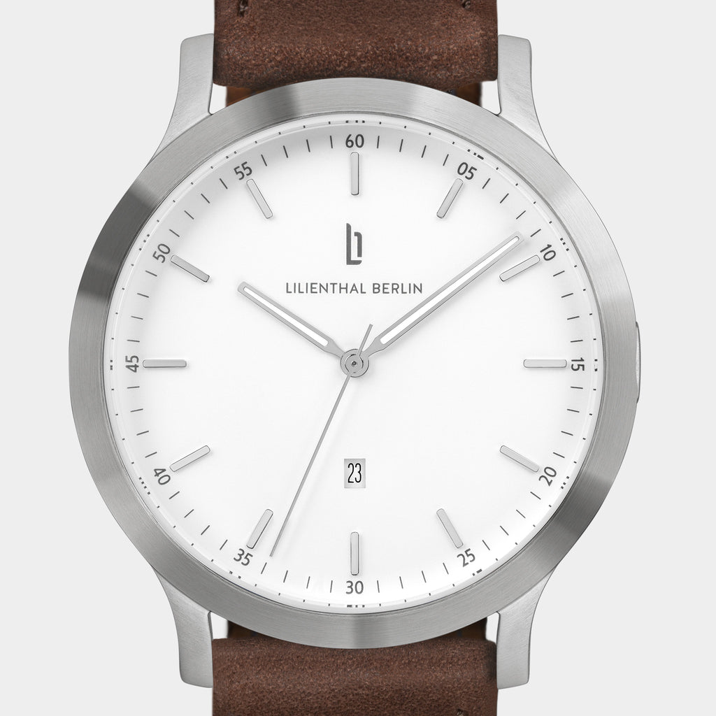 Minimalist silver wristwatch with white dial, date display, and brown leather strap