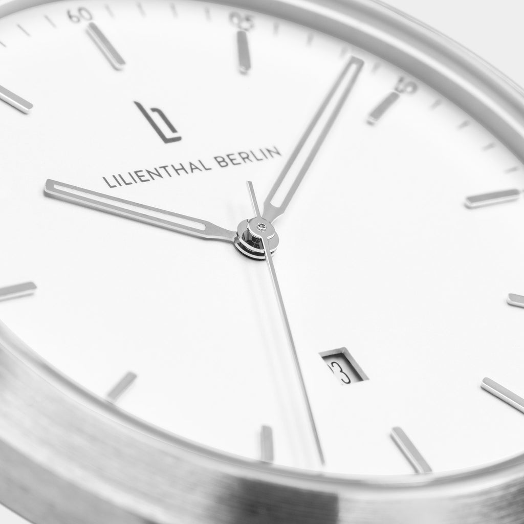 Close-up of a minimalist silver watch face with date display and white dial.