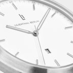 Close-up of a minimalist silver watch face with date display and white dial.