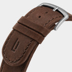 Close-up of brown leather watch strap with silver buckle and embossed detail