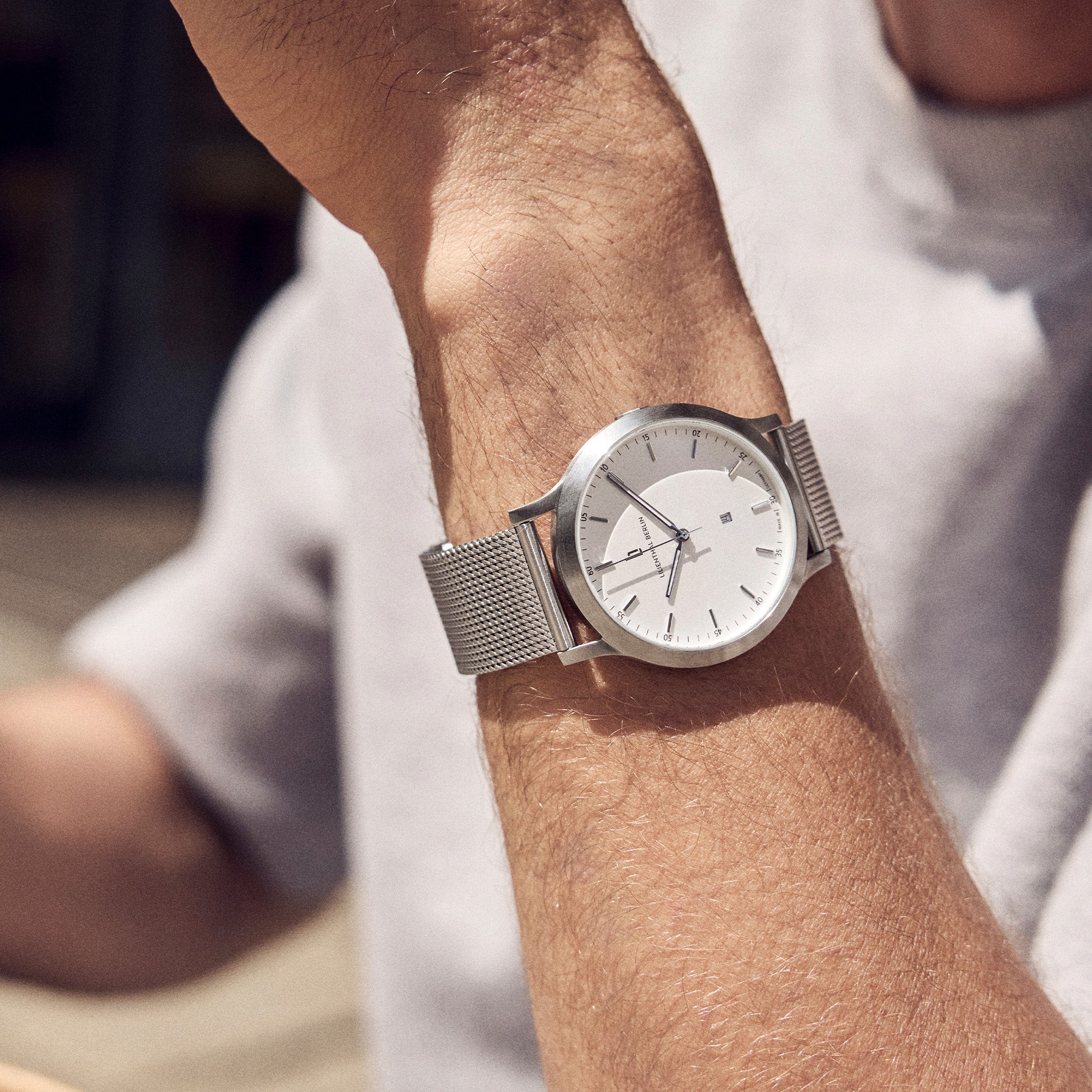 Minimalist silver mesh men's wristwatch with white dial on wrist outdoors