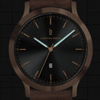 Minimalist black and bronze analog wristwatch with brown leather strap and date display