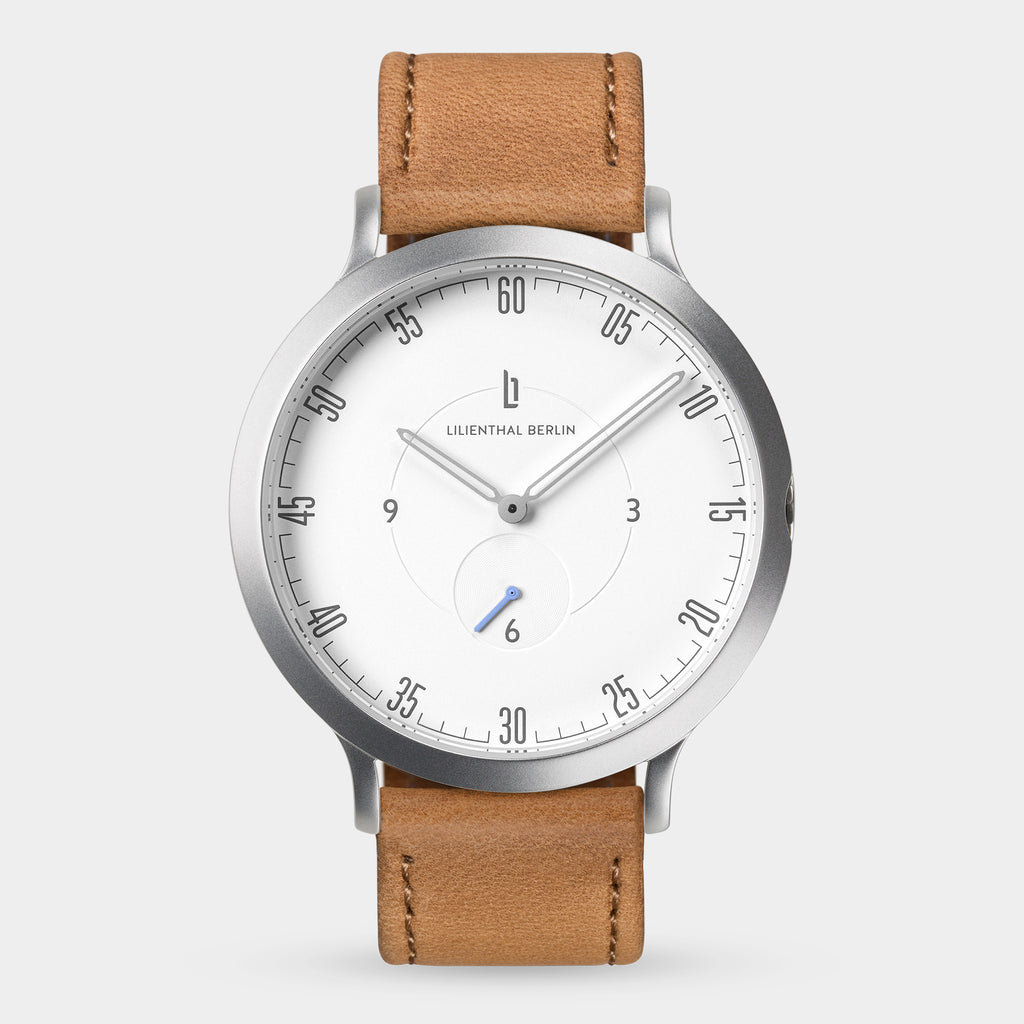 Minimalist watch with white dial, tan leather strap, and silver case on white background.
