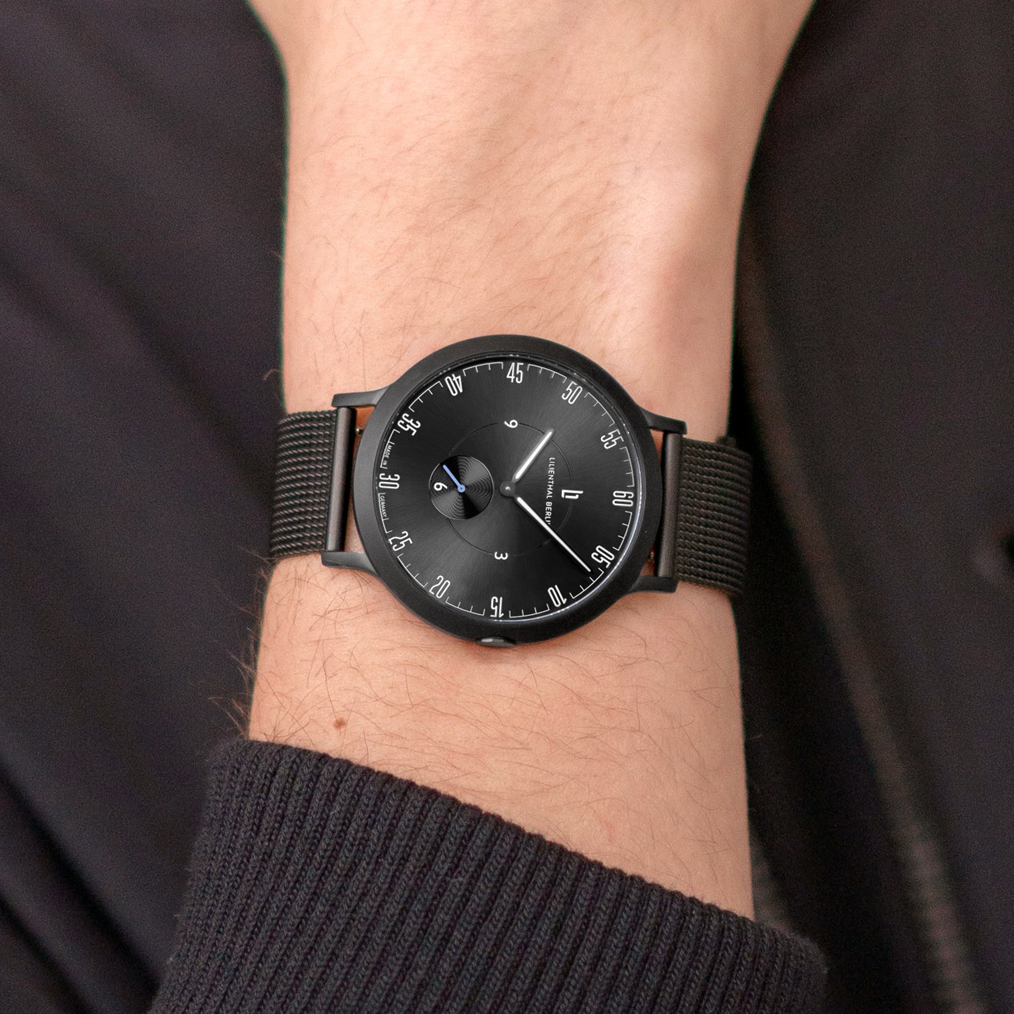 Minimalist black wristwatch with mesh strap on wrist, modern analog watch design