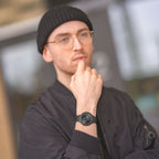 Man in black beanie and glasses wearing a modern black wristwatch outdoors