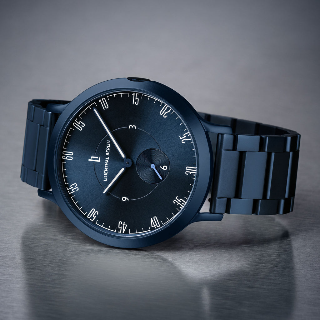 Matte black minimalist wristwatch with metal link strap and modern dial on grey surface.