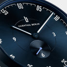 Close-up of a minimalist blue watch face with luminous hands and subdial.