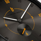 Close-up of a black watch dial with orange numerals and white luminous hands.