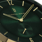Close-up of green watch face with gold hands and markers, modern minimalist design